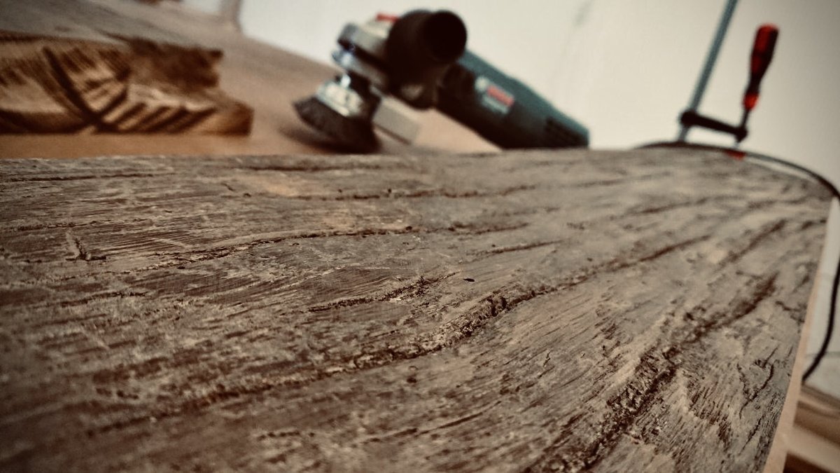 Weathered oak surface being brushed back, grinder and clamp behind